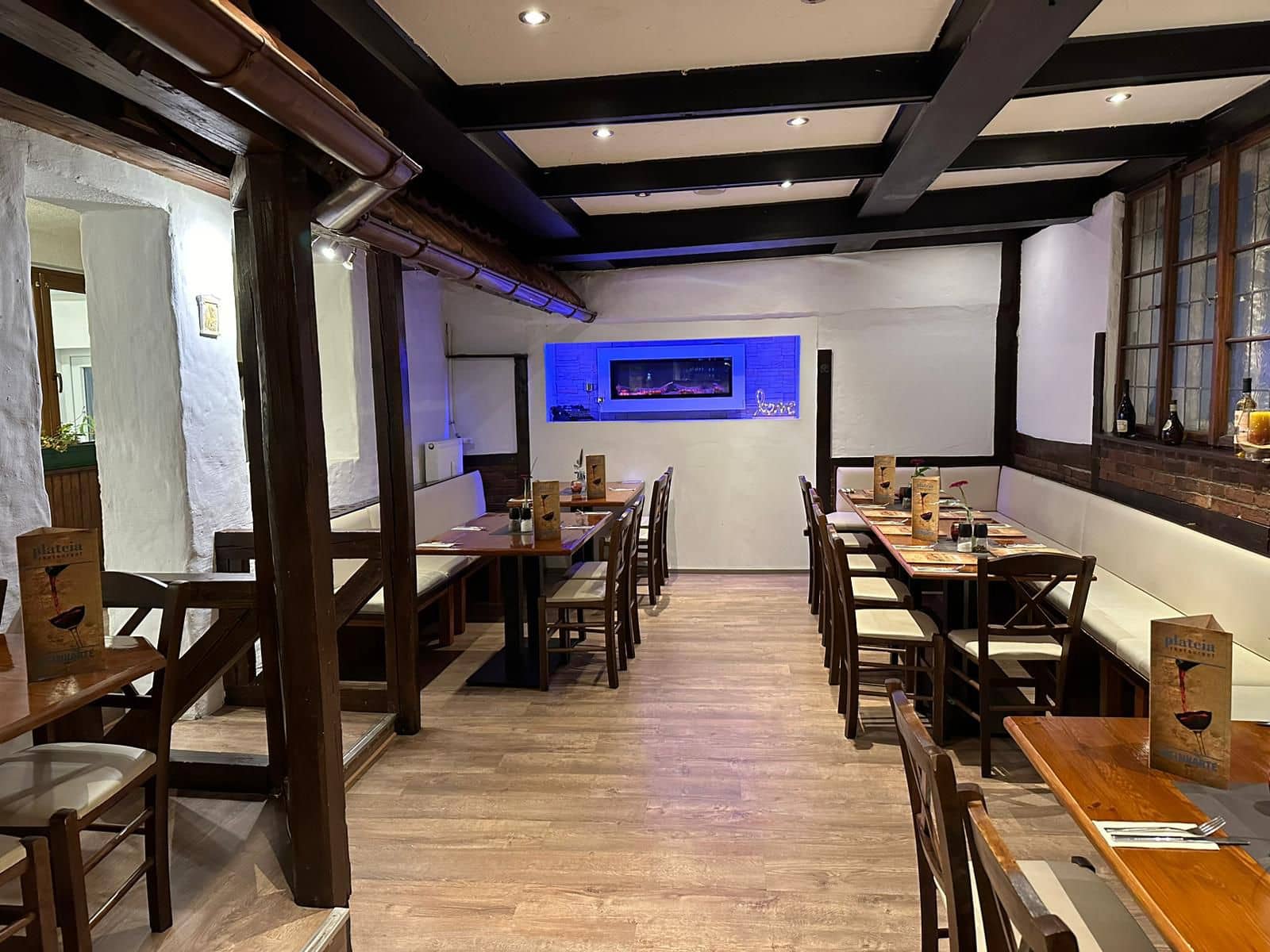 Das Foto zeigt den Innenraum eines leeren Restaurants mit Holztischen, Stühlen und Sitzbänken sowie sichtbaren Fachwerkbalken.