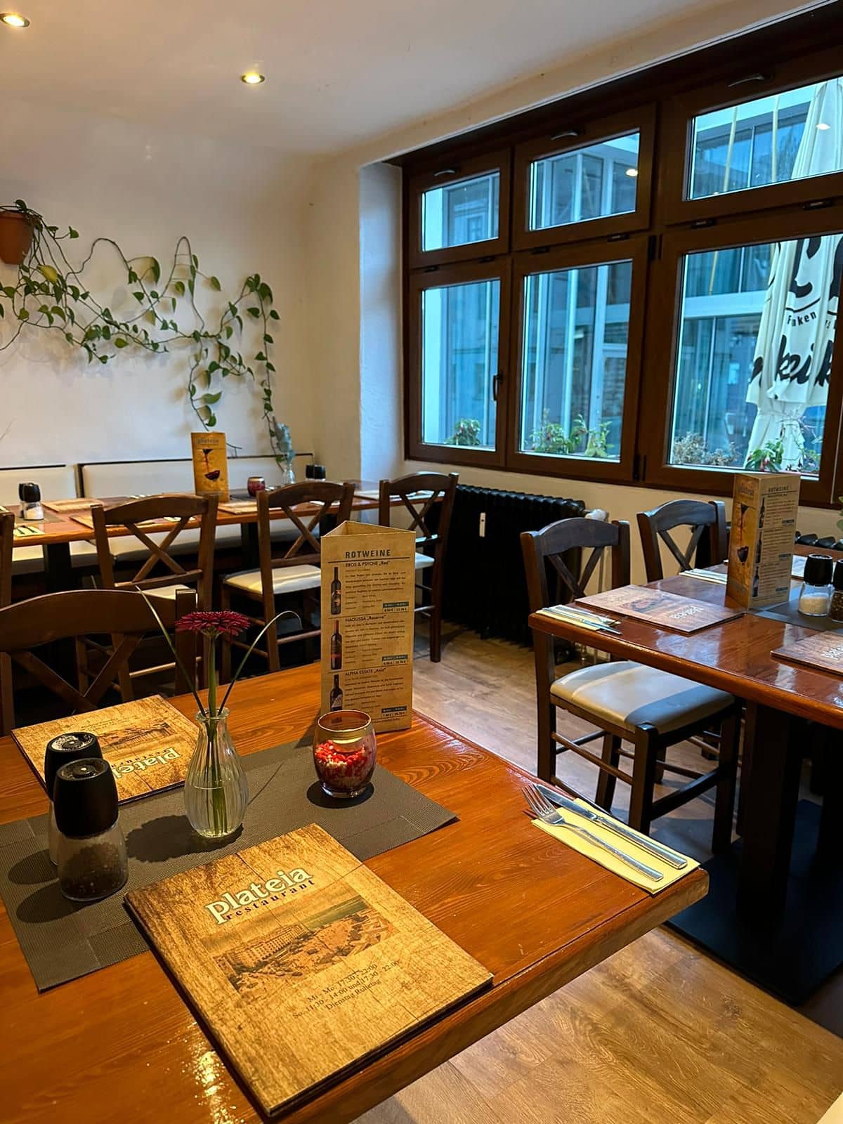 Das Foto zeigt das gemütliche Interieur eines Restaurants mit mehreren gedeckten Holztischen und Stühlen.