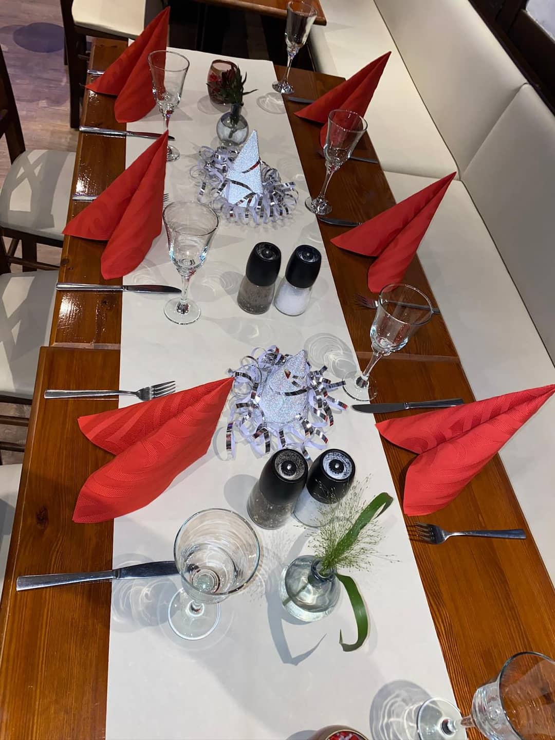Ein festlich gedeckter Holztisch in einem Restaurant mit roten Stoffservietten, Gläsern und Besteck.